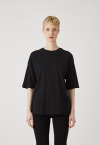 Tricou negru supradimensionat cu mâneci scurte, fabricat din bumbac. Prezentă un decolteu rotund și o croială relaxată, purtat cu colanți negri.
