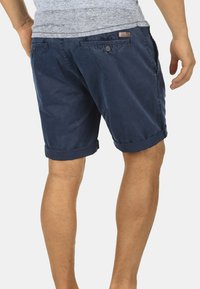 Shorts en coton bleu marine avec ourlets retroussés, dotés de deux poches arrière et d'une étiquette de marque discrète près de la taille. Texture lisse.
