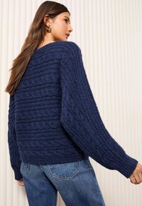 Mornarsko pleteni pulover z teksturiranim kablom, širokimi rokavi in sproščenim krojem. V kombinaciji z modrimi traper jeans.