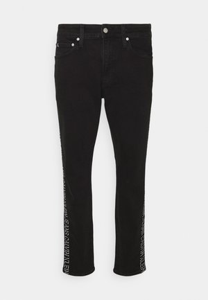 Jean slim noir avec bouton argenté, poches avant et logo Calvin Klein blanc le long des coutures latérales extérieures.