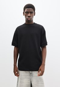 Tricou negru supradimensionat cu mâneci scurte și decolteu rotund, realizat dintr-un material neted, solid, asortat cu pantaloni scurți din denim gri deschis.