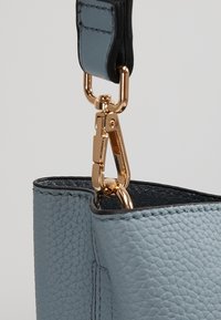 Lichtblauwe leren tas met een gestructureerd oppervlak, zwarte schouderband en gouden sluiting. Open bovenkant met zichtbare binnenvoering.