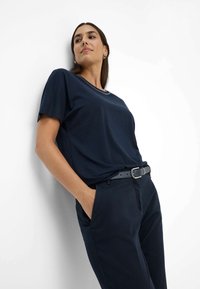 Marineblå t-shirt med korte ærmer og rund halsudskæring, lavet af blødt stof. Har en afslappet pasform, parret med mørke bukser og et sort bælte.