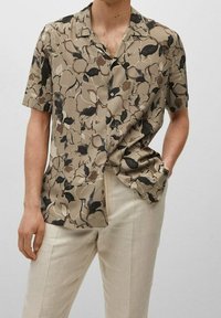 Chemise à manches courtes en tissu léger beige et marron avec des motifs abstraits de feuilles ; présente une coupe décontractée et un col ouvert.