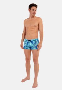 Badehose in Blau und Türkis mit floralem Muster, ausgestattet mit einem Kordelzug und einer figurbetonten Passform. Glatte Stofftextur.