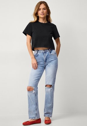 Black cropped t-shirt, light blue distressed jeans with ripped knees, and red flats. Simple design with a relaxed fit and soft texture.