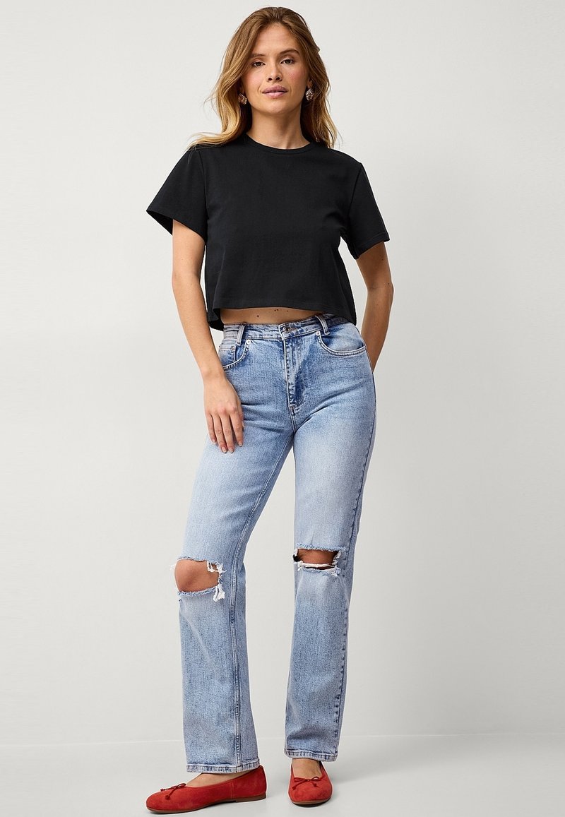 Zwarte cropped t-shirt, lichtblauwe distressed jeans met gescheurde knieën en rode ballerina's. Eenvoudig ontwerp met een ontspannen pasvorm en zachte textuur.