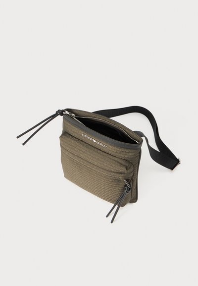 Borsa a tracolla verde oliva realizzata in materiale texturizzato, con chiusura zip, tasca frontale e tracolla regolabile con dettagli a nappina.