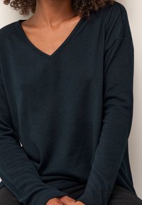 Ciemnoniebieski sweter w serek wykonany z miękkiej dzianiny. Posiada długie rękawy i luźny krój. Prosty design bez widocznych wzorów i dodatków.