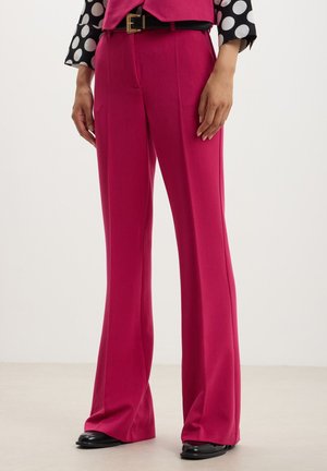 Pantaloni su misura fucsia realizzati in tessuto liscio, caratterizzati da un taglio a gamba larga e dettagli di pieghe, abbinati a scarpe nere.