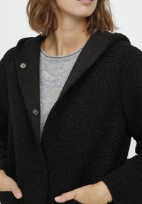 Fekete, texturált pulóverkabát puha fleece anyagból, szürke bélésű, széles gallérral és gombos záródással.