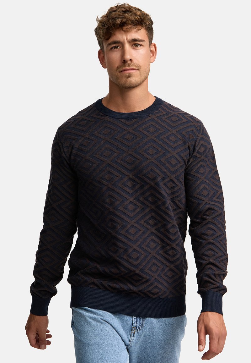 Pull marine bleu présentant un motif en losanges géométriques en relief. Les poignets et l'ourlet côtelés apportent de la texture et définissent la silhouette.