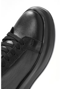 Sneaker in pelle nera con superficie testurizzata, lacci neri piatti e punta arrotondata. Presenta una suola in gomma nera spessa.