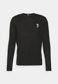 Pull-over noir à manches longues et col rond avec une petite figure de dessin animé portant des lunettes de soleil et une queue de cheval blanche sur la poitrine gauche.