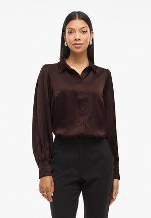 Bruine satijnen blouse met een kraag, knoopsluiting en lange mouwen. Glad textuur met een lichte glans, gedragen met zwarte op maat gemaakte broek.