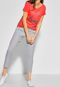 Červené tričko s krátkým rukávem se stříbrným potiskem "create with love", spárované s bledě šedými kostkovanými kalhotami a bílými teniskami.