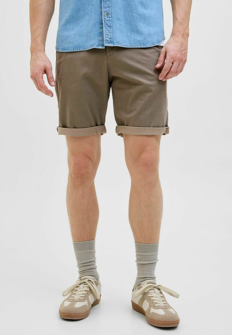 Brune shorts med opfoldede manchetter, lavet af letvægtsstof. Parret med lysegrå sokker og afslappede sneakers med beige og hvide accenter.