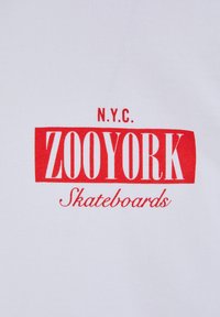 White fabric T-shirt featuring red text, "N.Y.C. ZOOYORK Skateboards," with a bold rectangular design and contrasting script.