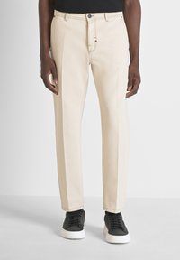 Pantalones rectos beige con frente plano, lazos para cinturón y un sutil detallado de costura, combinados con zapatillas negras.