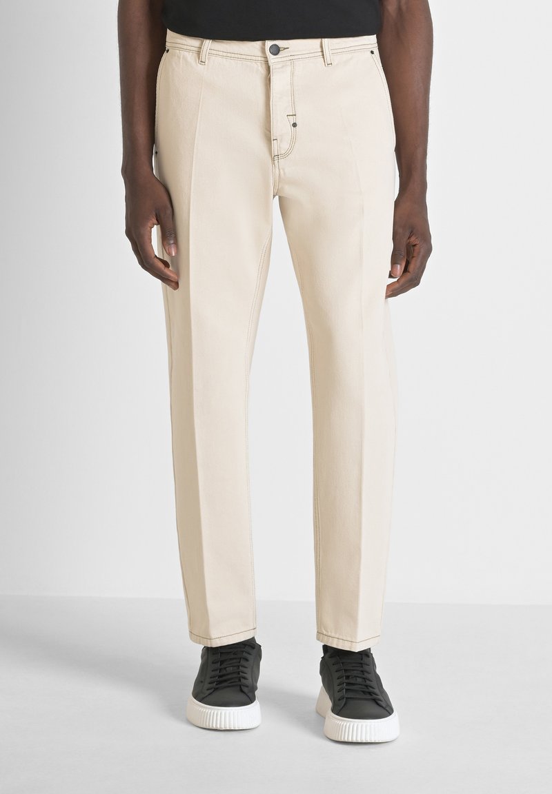 Pantalones rectos beige con frente plano, lazos para cinturón y un sutil detallado de costura, combinados con zapatillas negras.