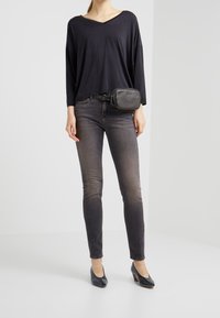 Top negro de manga larga con escote en V, combinado con jeans ajustados oscuros y zapatos de tacón negros brillantes. Pequeño bolso negro tipo bandolera sujetado en la cintura.