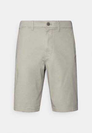 Short beige clair mi-long jusqu'aux genoux avec fermeture par bouton, passants pour ceinture et poches avant, présenté sur un fond uni.
