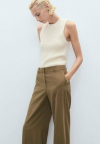 Krämfärgad ribbad ärmlös topp i kombination med högmidjade, löst sittande bruna byxor. Slät textur och rak silhuett.