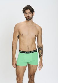 Boxer in cotone verde con una vita nera etichettata "RISPETTA". Il tessuto appare liscio e aderente, con una forma fitted.