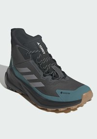 Czarno-błyszczące buty trekkingowe GORE-TEX z wysokim kostkiem, teksturowaną cholewką, trzema szarymi paskami po boku oraz solidną podeszwą.