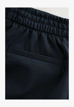 Dunkelblauem Stoff mit glatter Oberfläche. Verfügt über einen elastischen Bund und eine Paspeltasche, die Funktionalität mit einem minimalistischen Design verbindet.