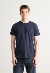 T-shirt en coton bleu marine à manches courtes et col rond. Présente un petit accent rayé à l'ourlet. Coupe décontractée.