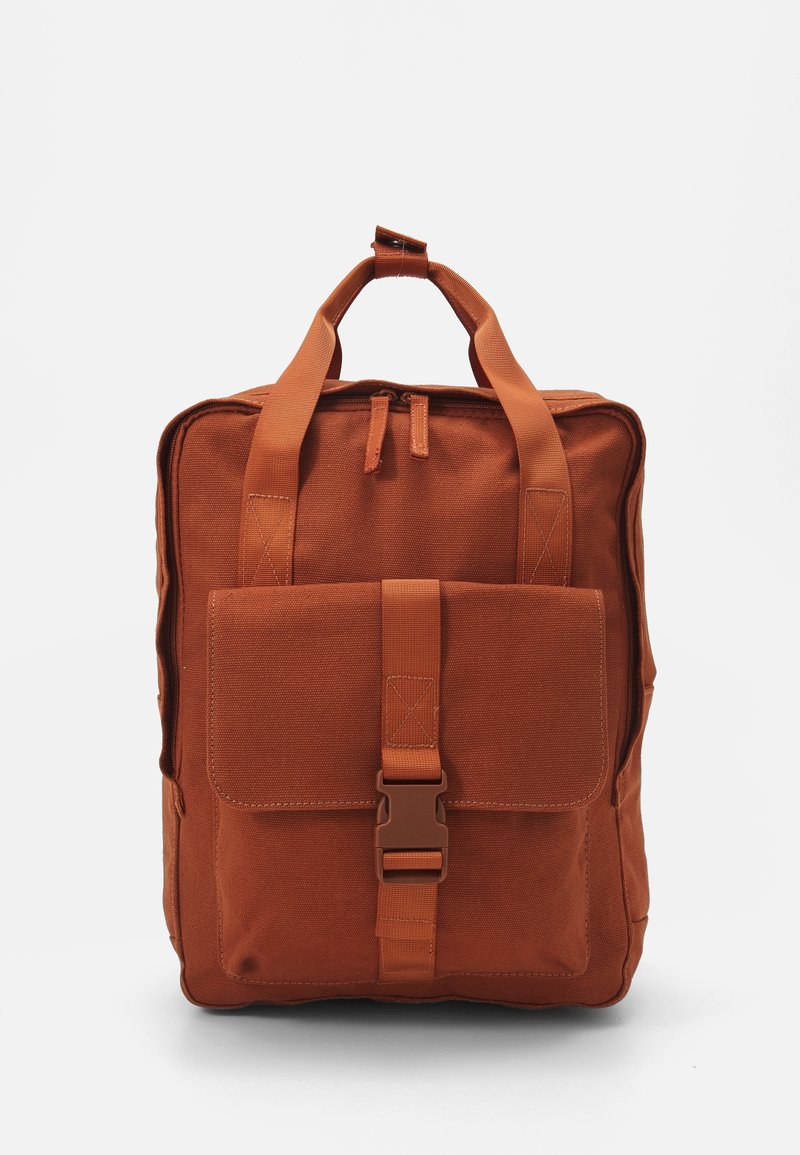 Sac à dos carré marron avec poignées supérieures, poche zippée à l’avant et rabat avant sécurisé par une boucle en plastique.