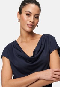 Navy blue top with a draped neckline and short sleeves, made of soft fabric, featuring a smooth texture and a relaxed fit.