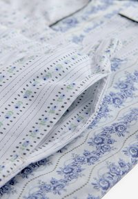 Plava i bijela tkanina s uzorkom koja prikazuje cvjetne dizajne i pruge. Tekstura je glatka s suptilnim varijacijama u boji i detaljima.