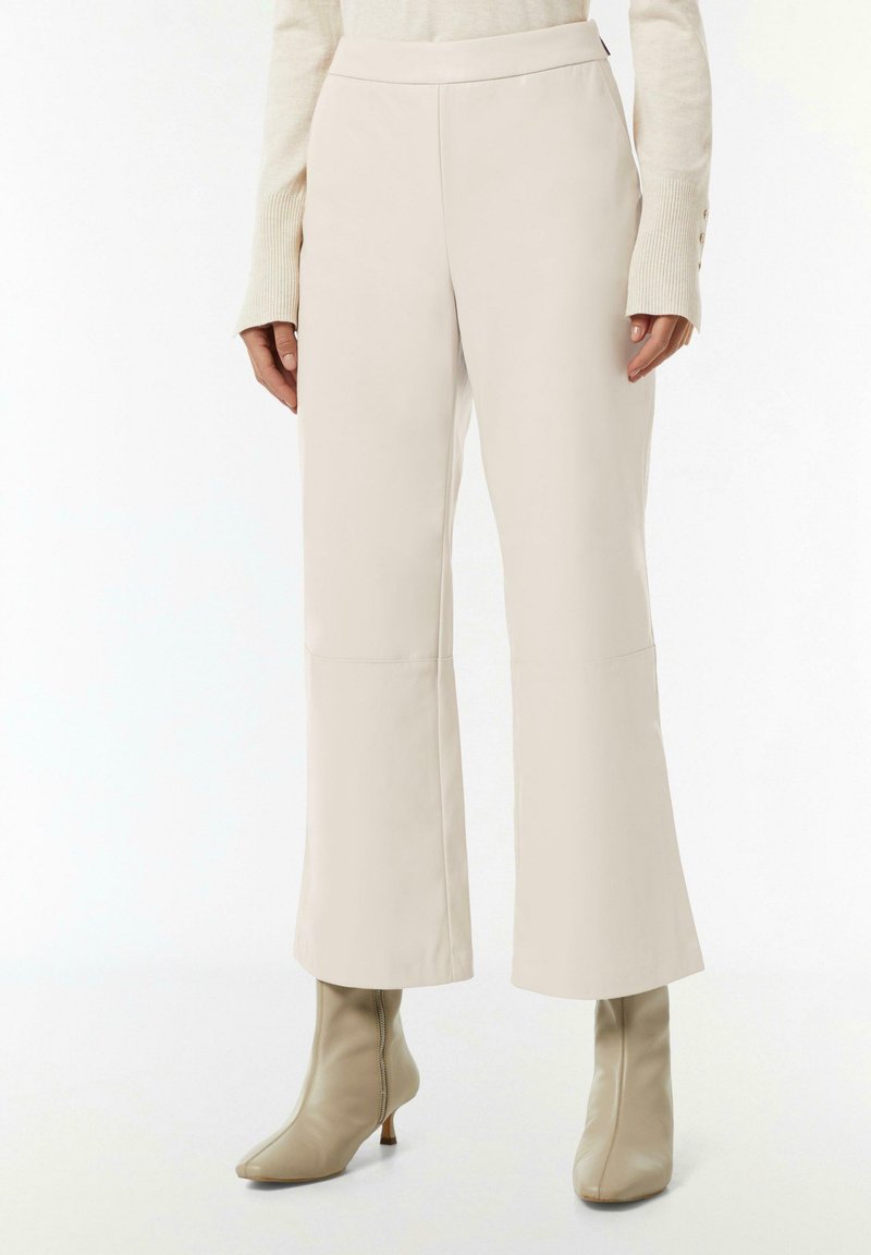 Beige taillierte Hose mit glatter Textur, weitem Bein und gestickten Details, kombiniert mit passenden Stiefeln mit Absatz und seitlichem Reißverschluss.