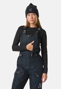 Czarny beanie i termiczny top w połączeniu z granatowymi śniegowymi ogrodniczkami z zamykanymi kieszeniami i regulowanymi paskami z akcentami logo.