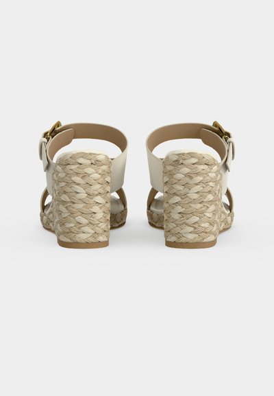 Sandales compensées beige avec talons en corde tressée, brides autour de la cheville et fermetures à boucle dorée, vues de dos sur fond blanc.