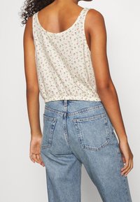Top de flores en tela color crema con pequeñas rosas rosas, cinturilla elástica y amplias sisas; combinado con jeans de mezclilla azul de tiro alto.