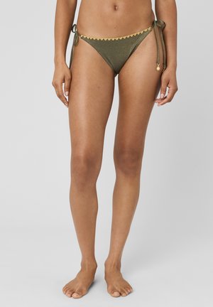 Femme portant un bas de bikini vert olive avec un bord festonné jaune et des liens latéraux ornés de petits charms en forme de soleil.