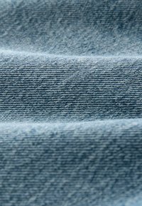 Ljusblå denimtyg med en slät, texturerad yta och en svag glans, kännetecknat av diagonala vävningsmönster.