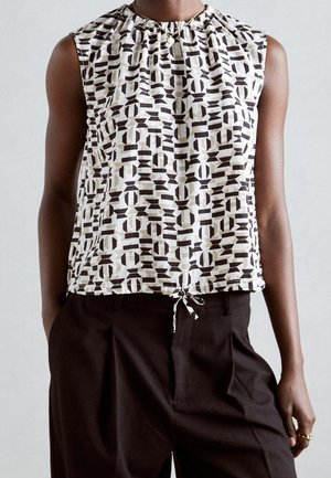 Top sin mangas con patrón geométrico en blanco y negro y bajo con cordón, combinado con pantalones plisados negros de cintura alta.