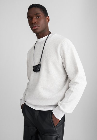 Light gray sweatshirt with a crew neck, complemented by a white undershirt, paired with black leather pants and a small black accessory pouch.