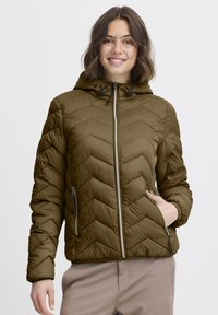 Alyvuogių žalios spalvos pūstinė striukė su gobtuvu, dekoruota chevrono formos siuvinėjimu, dviem šoniniais užtrauktukų kišenėmis ir reguliuojamais raišteliais prie gobtuvo.