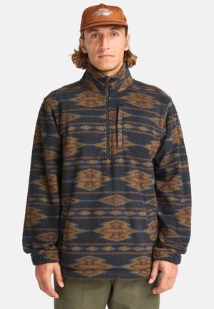 Fleece pullover met hoge kraag, gemusterd in donkerblauw en aardse tinten, voorzien van een borstzak en elastische manchetten.
