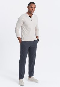 Beige Langarm-Henley-Shirt mit schwarzen und orangenen Knöpfen, kombiniert mit marineblauen tapered Hosen und hellgrauen Sneakers.