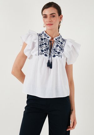 White blouse with ruffled short sleeves, embroidered floral pattern in navy, keyhole tie detail at the neckline, lightweight fabric.