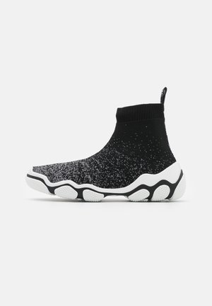 Zapatilla tipo calcetín en blanco y negro con parte superior de punto, cuello alto en el tobillo, lengüeta de tirador y suela texturizada ondulada en blanco y negro.