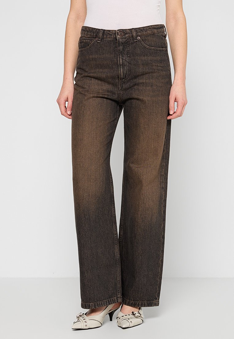 Frau trägt ausgebleichte schwarze weit geschnittene Jeans mit hoher Taille, kombiniert mit weißen, flachen, spitz zulaufenden Schuhen mit Metallelementen.