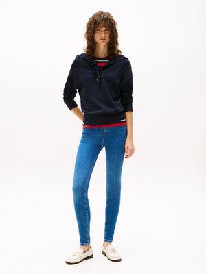 Marineblå hettegenser med snøring, med kabelstrikkdetaljer, kombinert med tettsittende blå jeans og beige loafers.