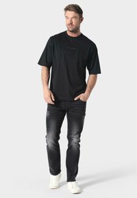 Camiseta negra de manga corta con un logo texturizado, combinada con unos jeans gris oscuro con un ligero desgaste y zapatillas blancas.